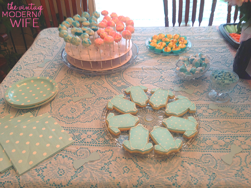 The blue side of this gender reveal table has blue onesie cookies from Sweet Elise bakery in Austin, Texas, pink and blue cake pops, blue deviled eggs, candies, and plates with napkins. Perfectly simple!