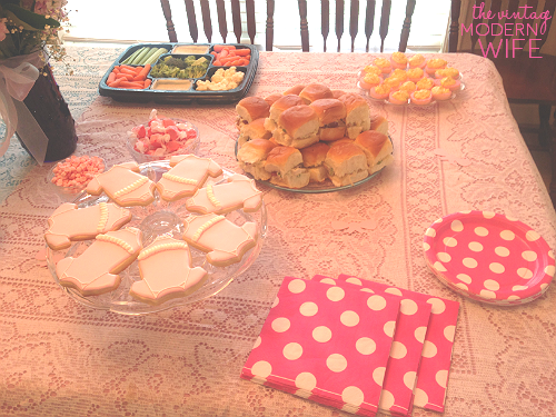 The pink side of this gender reveal able has pink onesie cookies from Sweet Elise bakery in Austin, Texas, pink deviled eggs, sandwiches and veggies, and plates with napkins. So cute!