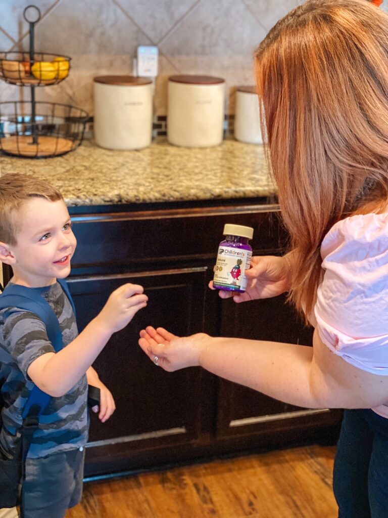 A young boy is smiling at his mom while he grabs a Standard Process vitamin from her hand. He is wearing a navy striped shirt with monster trucks on it